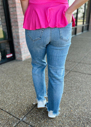 Woman walking in high-rise wide straight jeans with frayed hem and bright pink top.