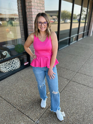 Woman wearing distressed wide straight jeans with ripped knees and frayed hem, paired with pink top and white sneakers.