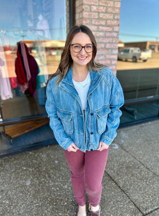 Woman wearing oversized denim jacket with pocket details, standing outdoors in casual outfit with glasses.