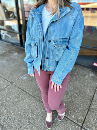 Woman wearing oversized denim jacket with multiple pockets, pink sweatpants, and white sneakers on sidewalk.