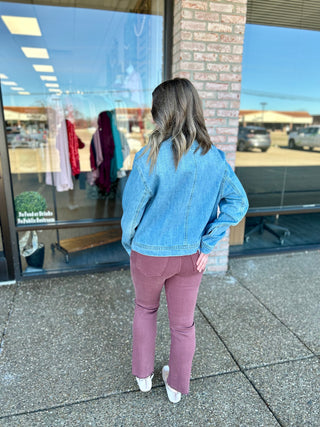 Woman wearing denim jacket and pink pants standing outside boutique storefront, viewed from behind.