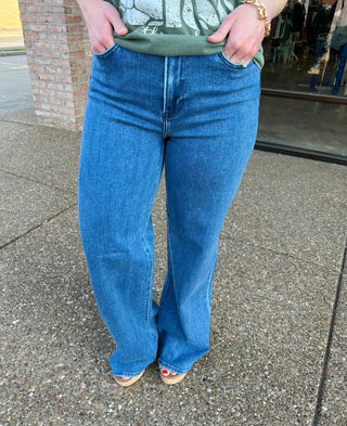 Woman wearing medium wash wide leg palazzo jeans standing on concrete sidewalk outside storefront