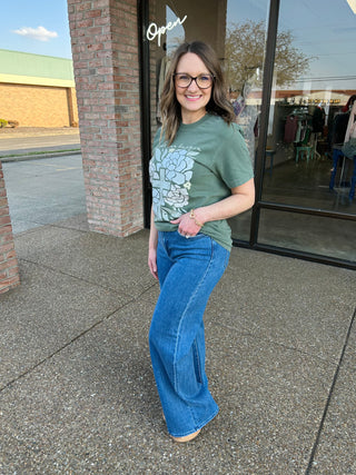 Woman wearing wide leg palazzo jeans and green floral t-shirt standing outside storefront
