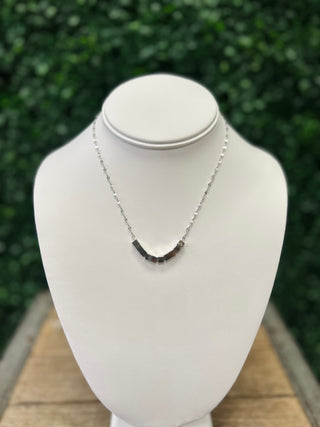 Silver chain necklace with geometric cube pendant displayed on white jewelry bust outdoors