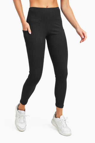 Woman wearing high-waisted dark gray ribbed leggings with side pocket and white sneakers on white background.