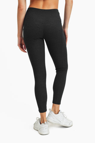 Woman wearing dark gray high-waisted leggings with white sneakers, shown from behind in athletic pose.
