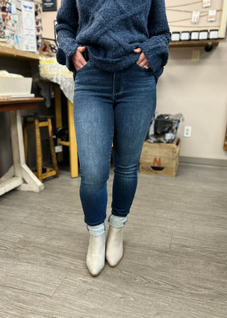 Person wearing dark wash skinny jeans with thermal sweater and beige ankle boots in casual indoor setting.
