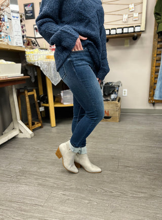 Woman wearing dark wash skinny jeans with oversized sweater and ankle boots in boutique setting.