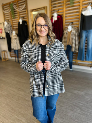 Woman wearing black and white plaid button-up shacket over dark top and jeans in clothing store