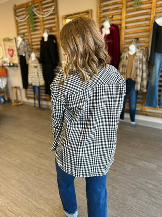 Woman wearing black and white plaid shacket with jeans, shown from behind in clothing boutique.