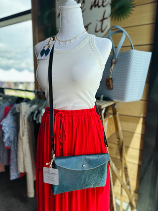 Mannequin wearing white tank top and red skirt displaying leather crossbody bag in boutique setting