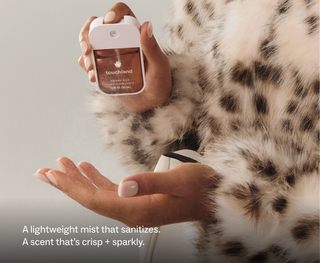 Touchland Power Mist hand sanitizer being sprayed onto an open palm, worn with a fur coat.