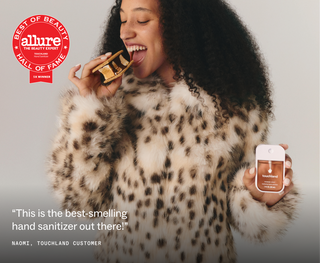 Woman in leopard coat holding Touchland Power Mist hand sanitizer while enjoying a s'more treat.