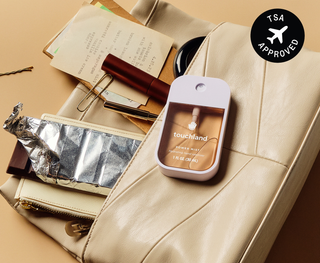 Touchland Power Mist hand sanitizer displayed on a leather bag with travel essentials, TSA approved.