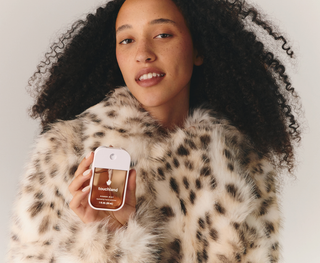 Woman in leopard fur coat holding Touchland Power Mist hydrating hand sanitizer spray bottle.