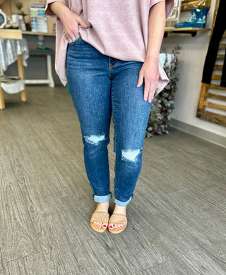 Woman wearing distressed midrise slim fit jeans with rolled cuffs and pink top in retail store