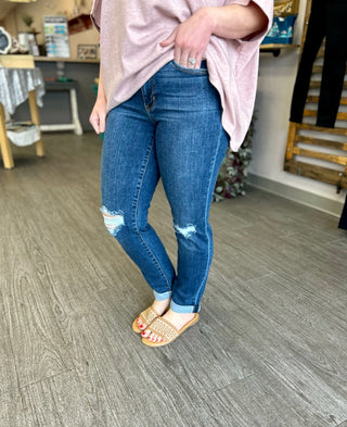 Woman wearing distressed slim fit jeans with rolled cuffs and pink top in casual indoor setting.
