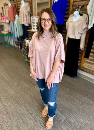 Woman wearing distressed denim jeans with pink top and sandals in clothing store setting.