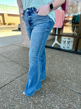 Person wearing Judy Blue midrise tummy control vintage flare jeans with light green top in outdoor setting.
