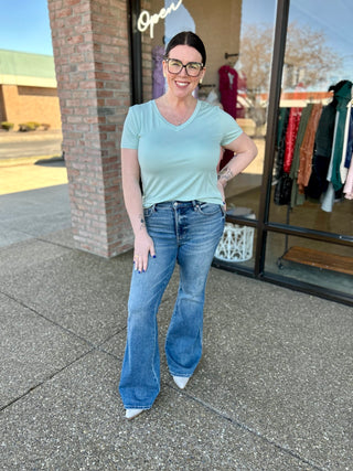 Woman wearing Judy Blue midrise tummy control vintage flare jeans with mint top outside boutique storefront.