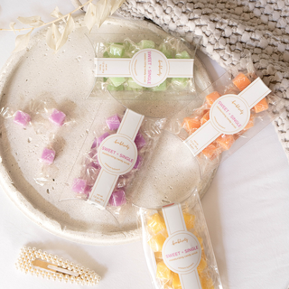 Bonblissity Sweet + Single moisturizing candy scrub cubes in clear packaging displayed on ceramic plate.
