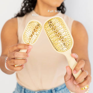 Woman holding two TELETIES vented hair brushes with gold bristles, showing mini and full size comparison.
