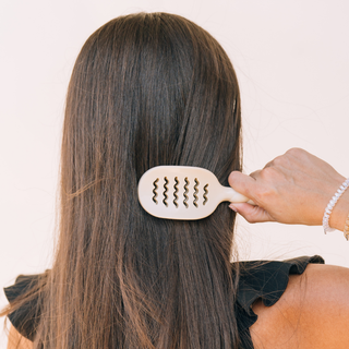 Woman brushing long brunette hair with a TELETIES Mini Vented Brush featuring wavy bristles.