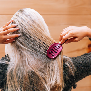 Person brushing long blonde hair with a small oval vented hair brush from behind.