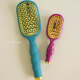 Two TELETIES vented hair brushes with gold bases and jeweled bristles displayed side by side.