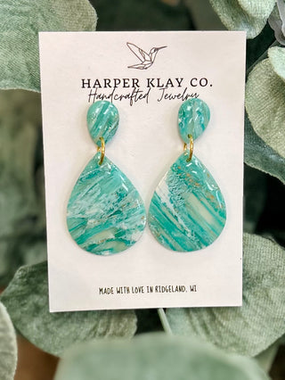Handcrafted drop earrings with marbled turquoise pattern displayed on white product card against green foliage background.