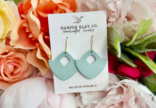 Mint green fan-shaped clay earrings on branded card surrounded by coral and white flowers