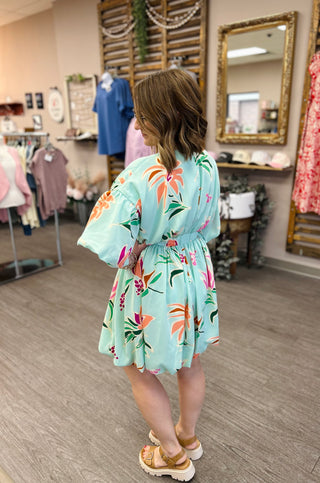 Woman wearing mint green floral print bubble dress with bell sleeves in boutique setting