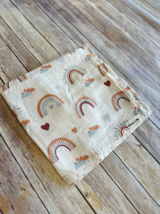 Soft baby blanket with rainbow and heart pattern on wooden deck surface