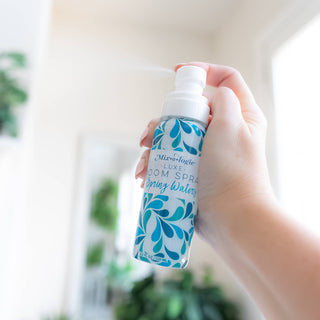 Hand holding Mixologie room spray bottle with blue water droplet design against blurred background