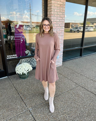 Woman wearing mocha mock neck sweater dress with long sleeves standing outside storefront.
