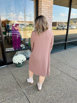 Woman wearing mocha mock neck sweater dress walking on sidewalk, showing back view of midi-length dress.
