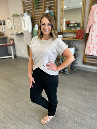 Woman wearing light gray asymmetrical top with black leggings in retail boutique setting