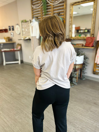 Woman wearing white asymmetrical top and dark pants in modern retail store setting.