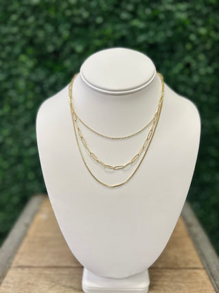 Gold layered necklace with mixed chain styles displayed on white jewelry bust stand outdoors.