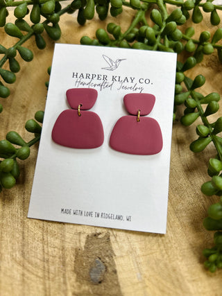 Handcrafted mulberry clay earrings on white display card surrounded by green succulent plants on wood surface.