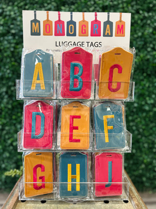 Colorful monogram luggage tags displayed in clear plastic organizer showing letters A through I