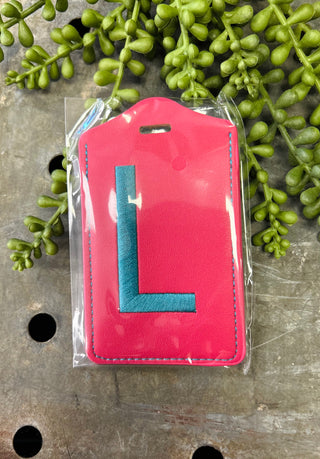 Pink leather luggage tag with blue monogram letter in clear protective packaging