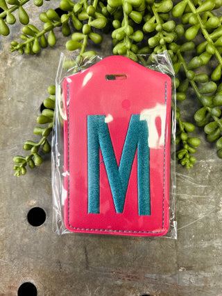 Pink leather luggage tag with blue monogram letter M in clear protective packaging