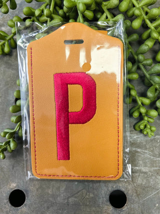 Monogram luggage tag with embroidered letter P in leather design, packaged in clear protective sleeve.