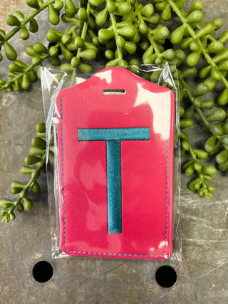 Red leather luggage tag with blue monogram letter T in clear protective packaging