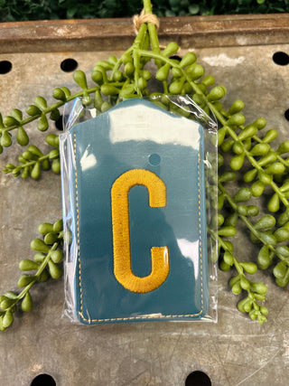Monogram luggage tag with embroidered letter on fabric material in clear protective packaging