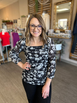 Woman wearing black and white floral ruched top with long sleeves in boutique setting