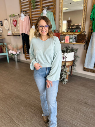 Woman wearing light blue oversized pullover sweater with jeans in boutique clothing store setting