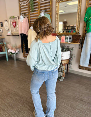 Woman wearing light blue pullover sweater and jeans in boutique clothing store setting