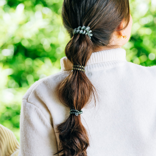 Person wearing TELETIES spiral hair ties styled in a cascading ponytail with green bokeh background.